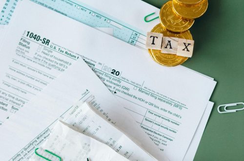 Tax documents and gold coins on a green desk symbolizing financial planning and savings.